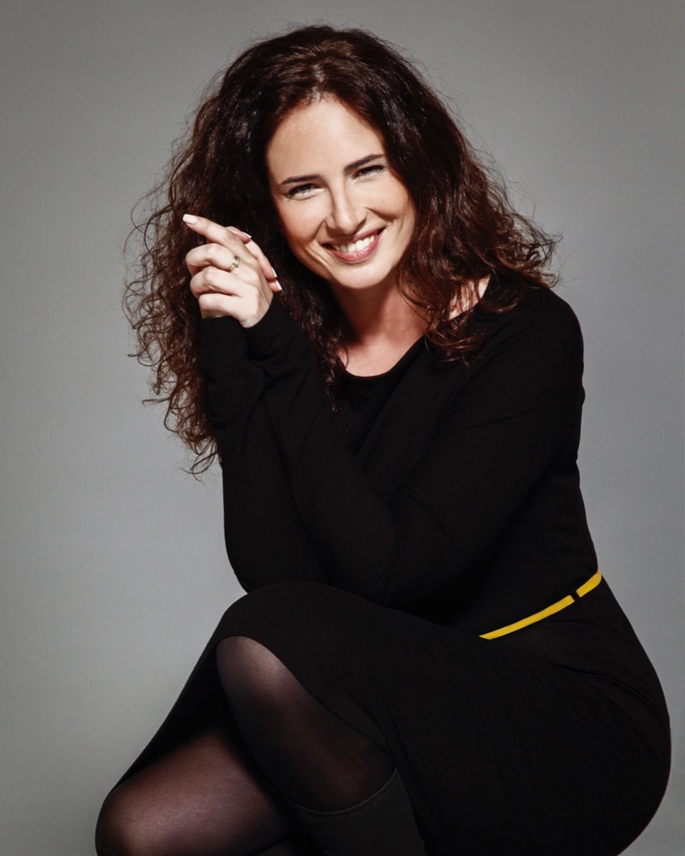 Retrato en color de Sandra María Rojas Montes, sonriente, con ropa negra y fondo gris