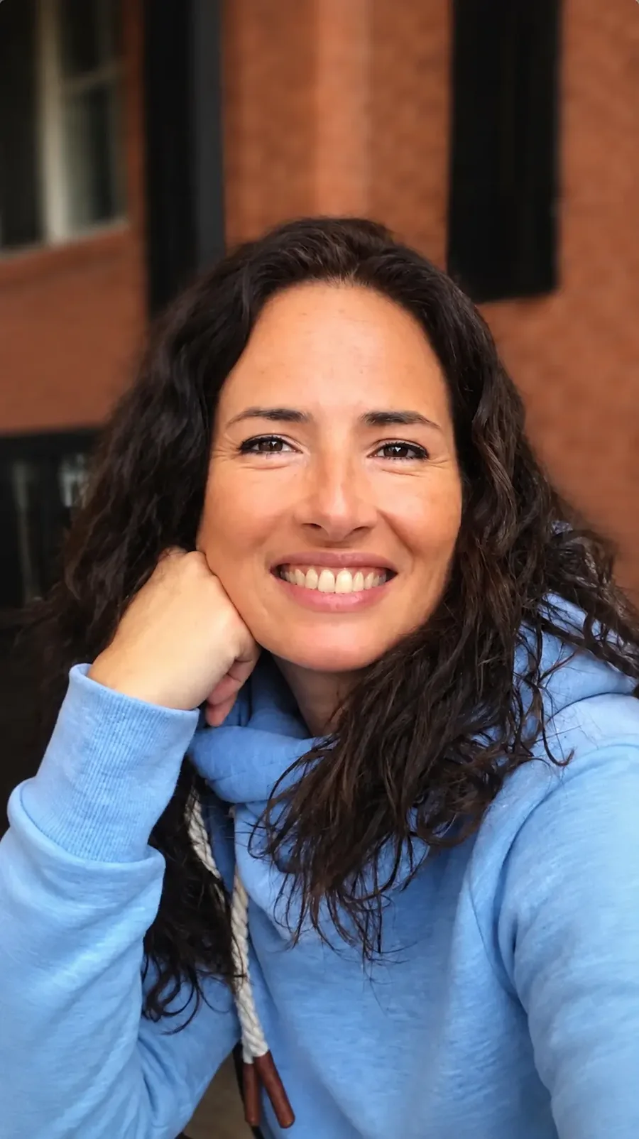 Retrato en color de Sandra María Rojas Montes, sonriente, con jersey azul y la mejilla apoyada en la mano